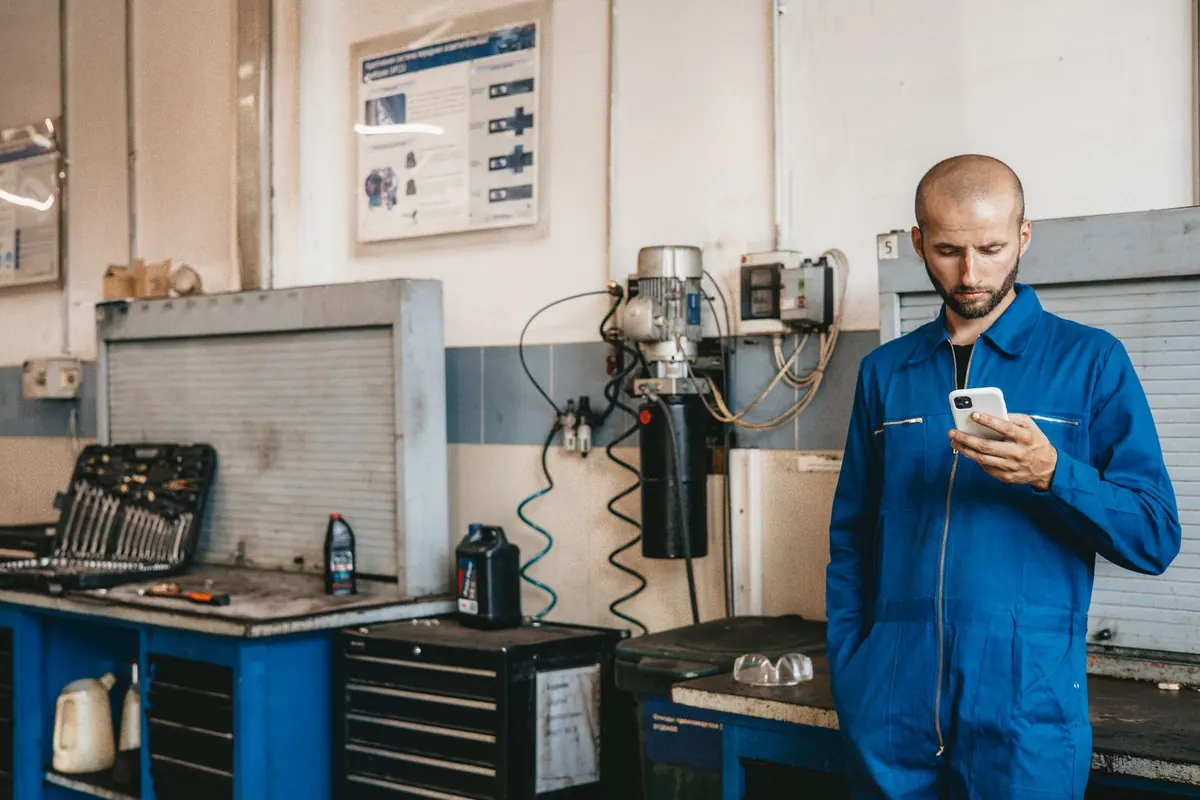 Tradesperson in blue work overalls checking his smartphone in a workshop